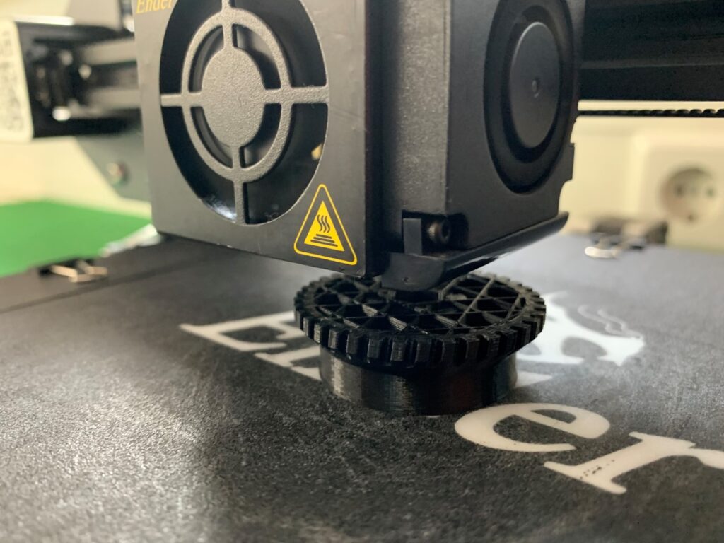 3D-printer in actie met het printen van een zwart tandwiel op een Ender-3 buildplate