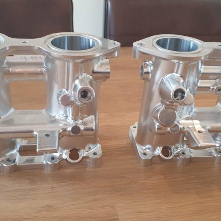 Twee aluminium CNC-gefreesde inlaathuizen voor motorsporttoepassing op houten ondergrond